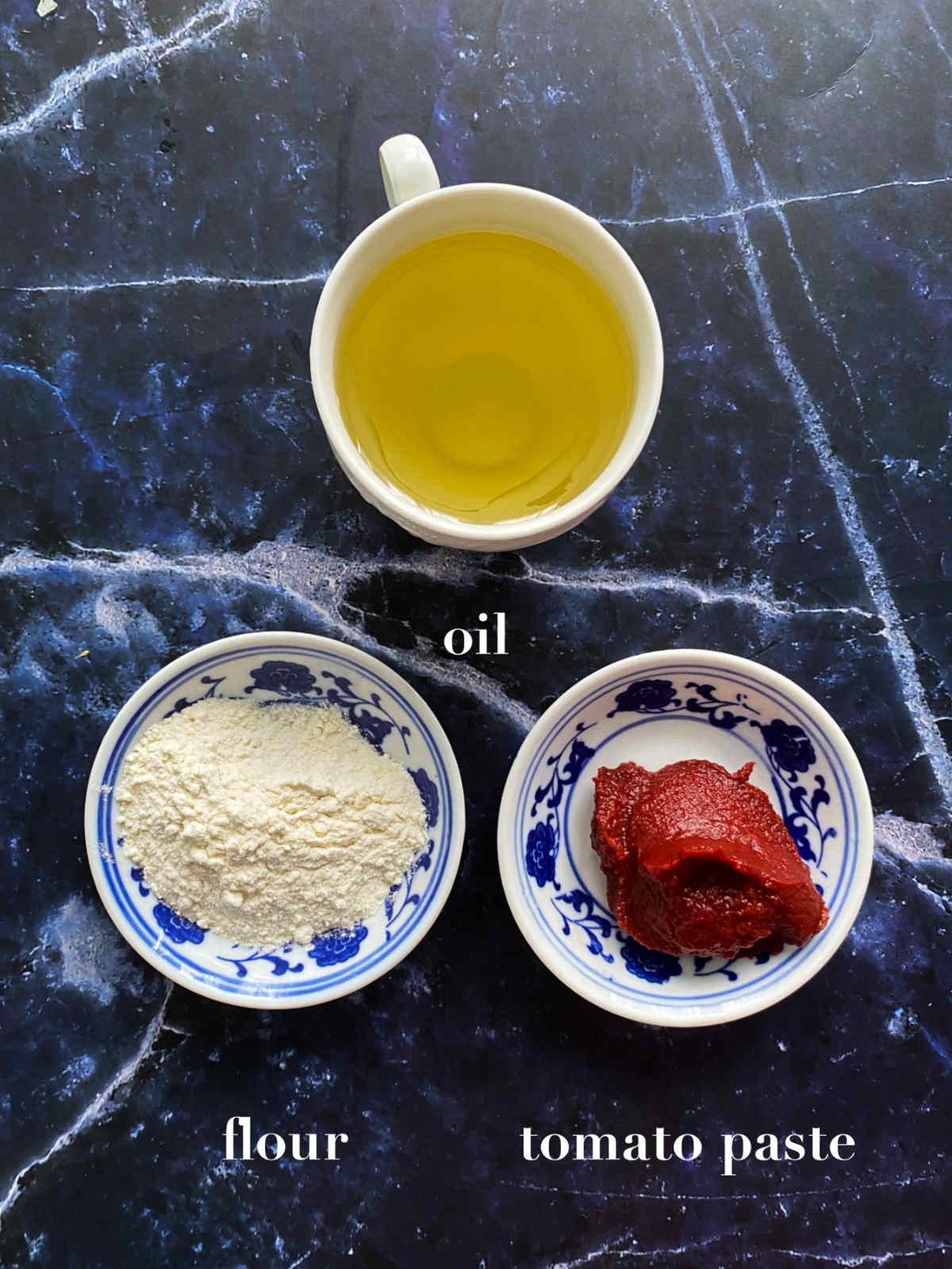 Roux ingredients (oil, tomato paste and white flour) on a dark blue background. 