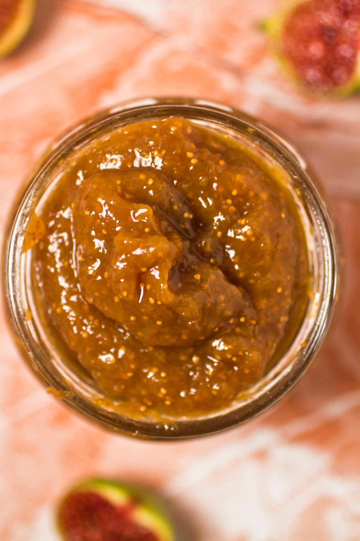 Fig jam in a jar from above, and a few fig halves on pink background.