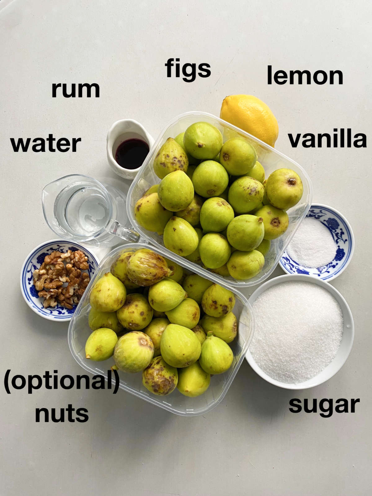 Ingredients overhead on a white table: figs, rum, water, nuts, lemon, vanilla.