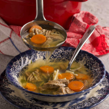 Red pot with soup, a ladle and a soup bowl with soup on a gray background (spoon and kitchen towel also included).